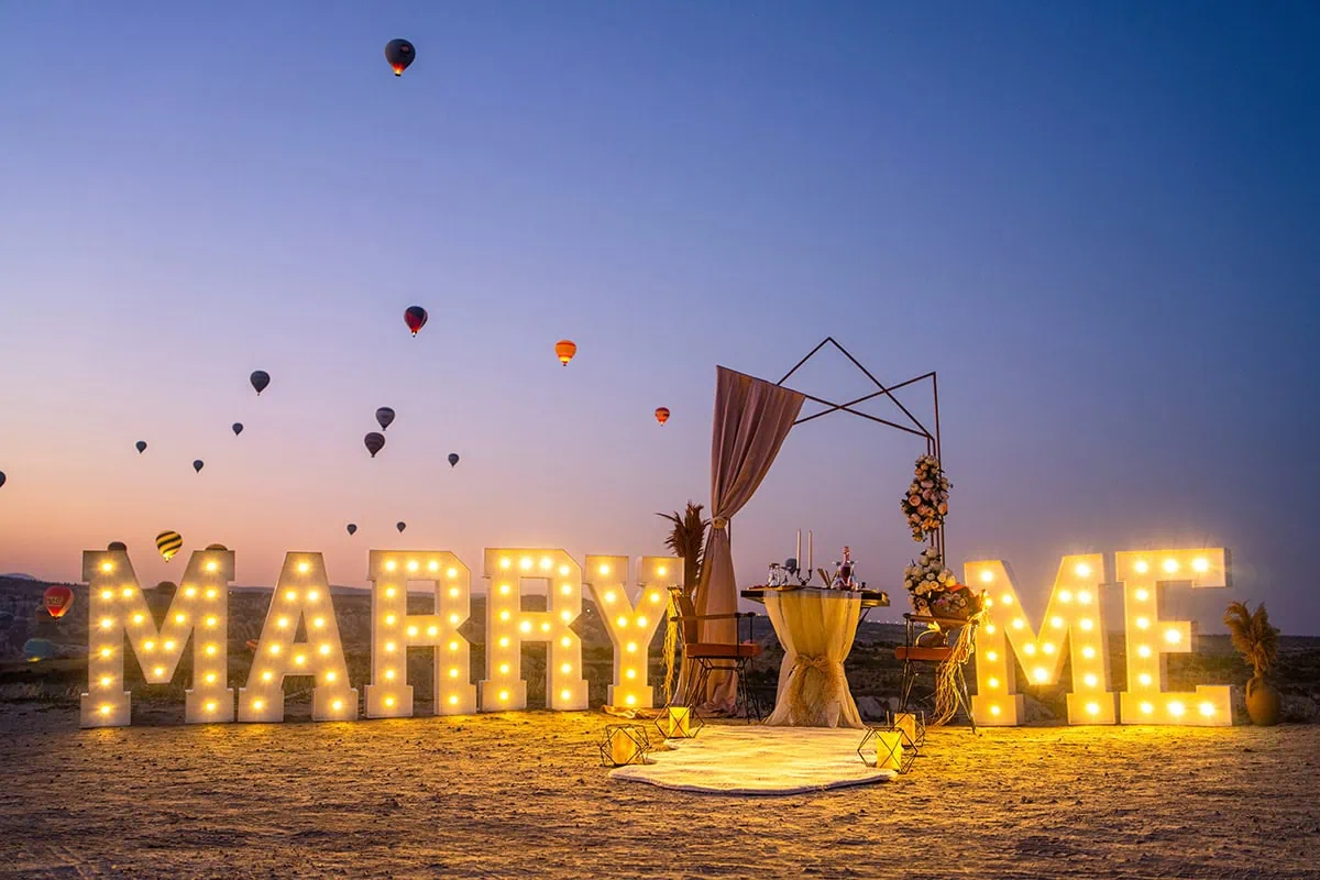 Alacakaranlikta isikli MARRY ME harfleri, perde dekoru ve balonlarla vadi manzarasi