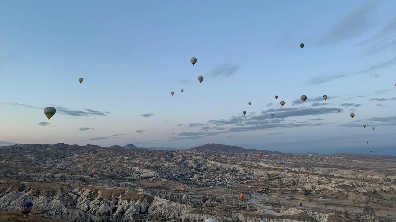 Kapadokya vadilerinin üzerinde şafak ışığında dağılmış onlarca sıcak hava balonu; hiçbiri yakın planda değil.