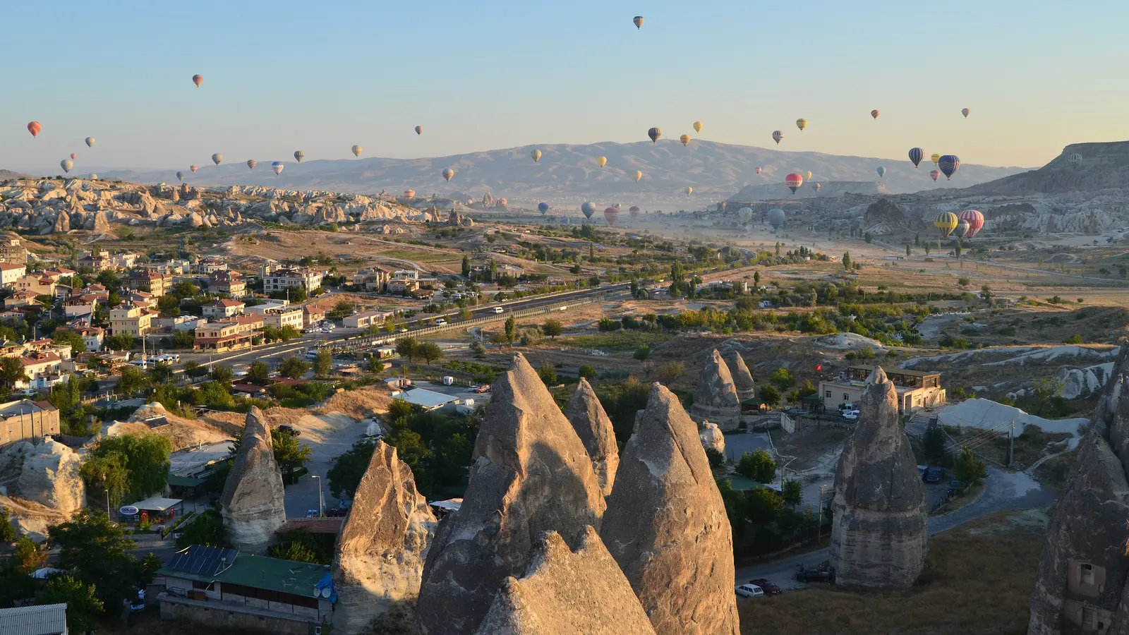 Göreme yakınında güneş doğarken kaya oluşumları üzerinde uçan sıcak hava balonları; temsili manzara.