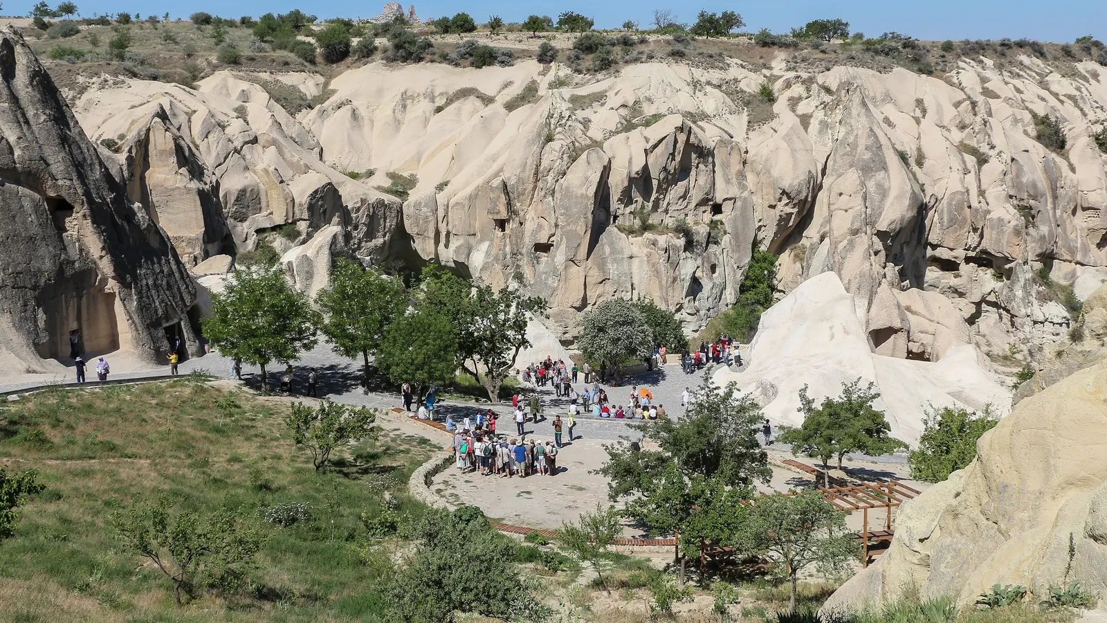 Göreme Açık Hava Müzesi’nin yukarıdan görünümü; kaya kiliselerin önündeki patika ve meydanda uzaktan görünen ziyaretçi grupları.