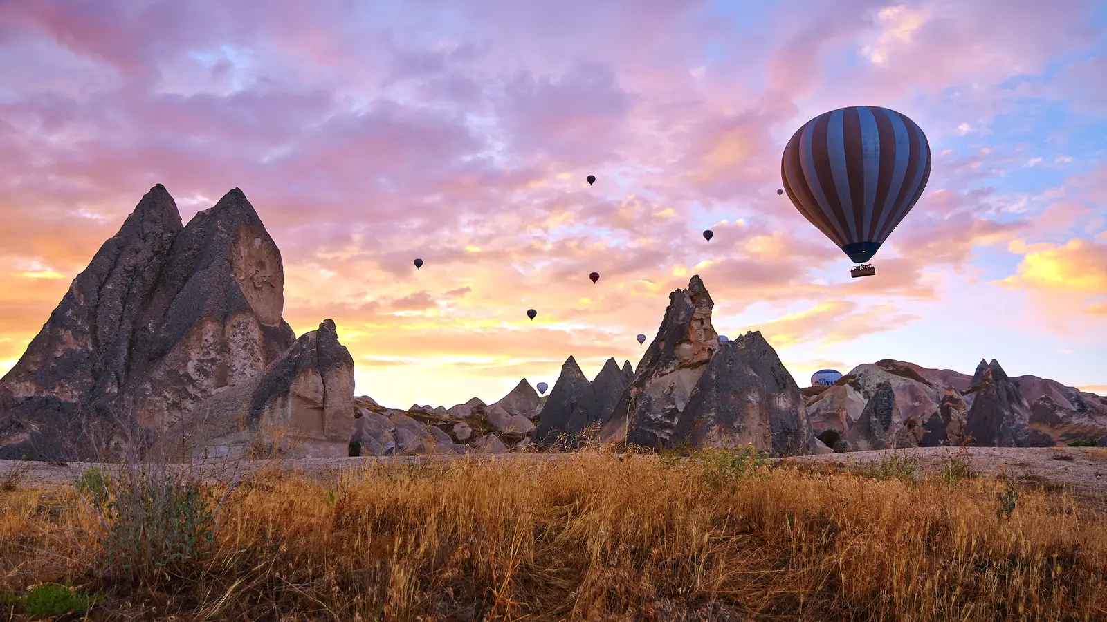 Göreme çevresinde gün doğumunda vadi manzarası ve sıcak hava balonları.